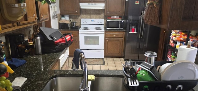 10623 White Oak Canyon Rd, Oklahoma City, OK 73162 - kitchen with under cabinet range hood, electric range, black fridge with ice dispenser, stainless steel microwave, and decorative backsplash