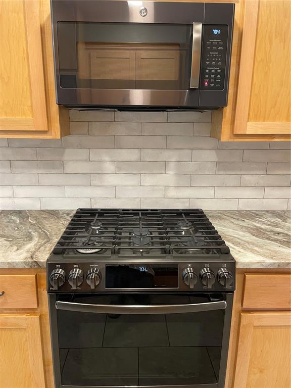 3017 Kelsey Dr, Edmond, OK 73013 - kitchen with black range oven, stainless steel microwave, backsplash, and light stone counters