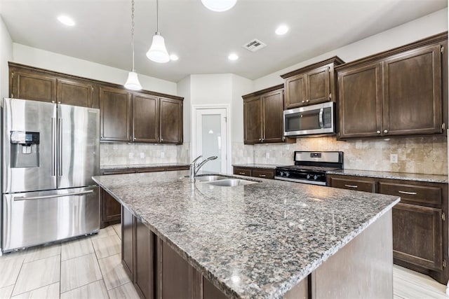 868 Phils Way, Piedmont, OK 73078 - kitchen with stainless steel appliances, dark brown cabinetry, a center island with sink, dark stone countertops, and decorative backsplash