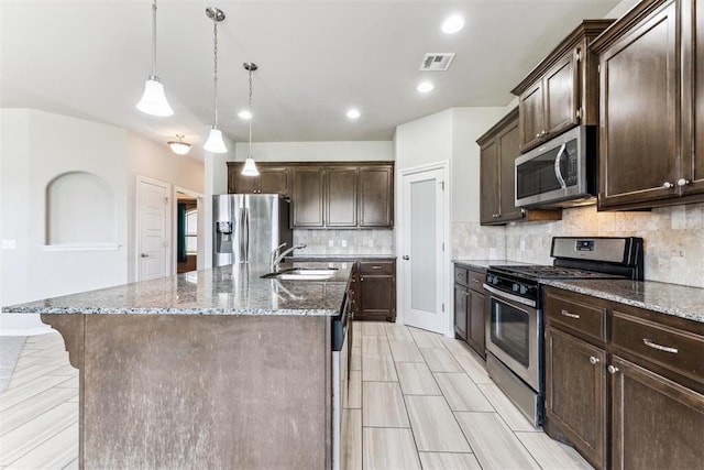 868 Phils Way, Piedmont, OK 73078 - kitchen with stainless steel appliances, dark brown cabinets, dark stone counters, backsplash, and an island with sink