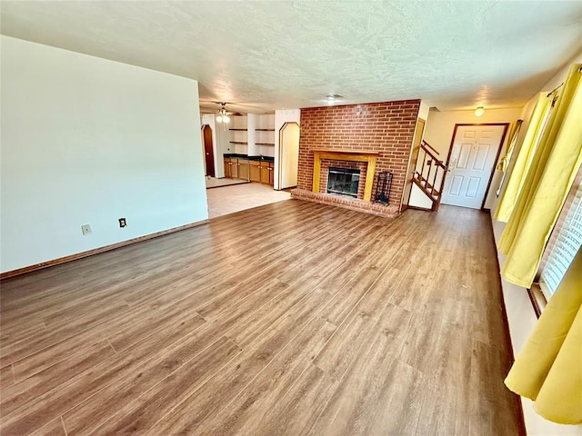 4400 Hemingway Dr Unit 263, Oklahoma City, OK 73118 - unfurnished living room featuring light wood finished floors, a brick fireplace, a textured ceiling, stairs, and baseboards