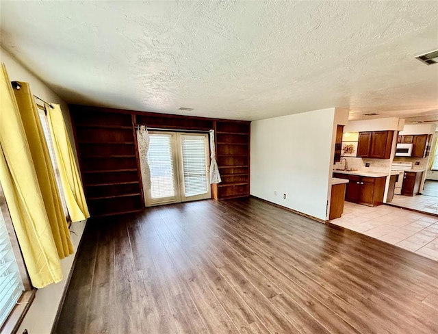 4400 Hemingway Dr Unit 263, Oklahoma City, OK 73118 - unfurnished living room with a textured ceiling, light wood-style floors, built in features, a sink, and baseboards