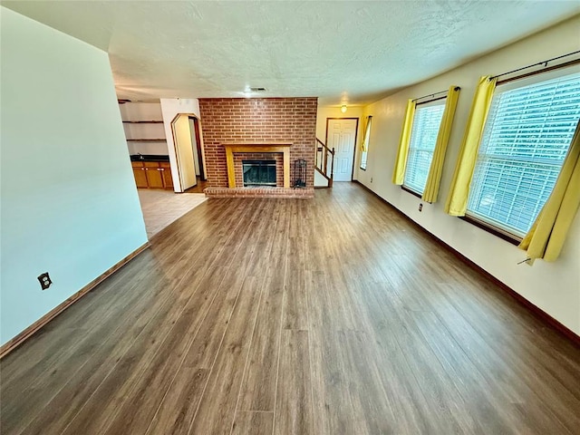 4400 Hemingway Dr Unit 263, Oklahoma City, OK 73118 - unfurnished living room with wood finished floors, a textured ceiling, a brick fireplace, and baseboards