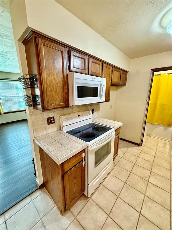 4400 Hemingway Dr Unit 263, Oklahoma City, OK 73118 - kitchen with white appliances, tile counters, light tile patterned floors, a textured ceiling, and baseboards