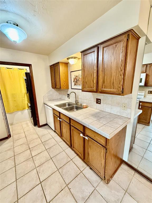 4400 Hemingway Dr Unit 263, Oklahoma City, OK 73118 - kitchen featuring a sink, white appliances, light tile patterned floors, backsplash, and brown cabinetry