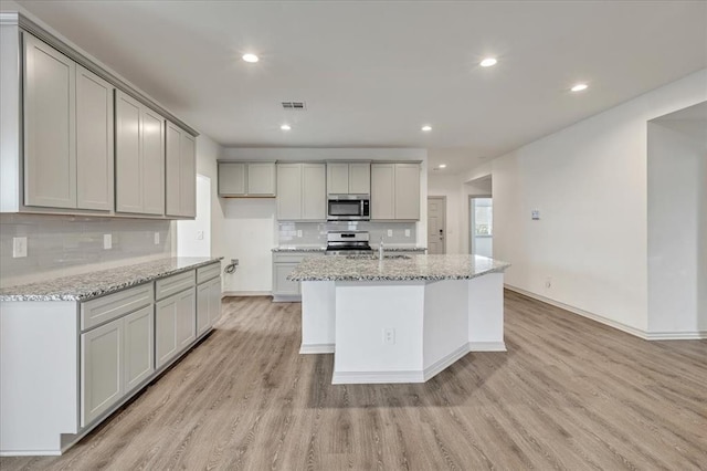 14500 Gravity Falls Ln, Oklahoma City, OK 73142 - kitchen featuring stainless steel appliances, light wood-style floors, tasteful backsplash, recessed lighting, and light stone countertops