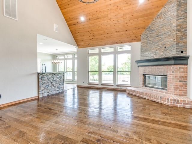 3805 Highridge, Edmond, OK 73003 - unfurnished living room featuring high vaulted ceiling, hardwood / wood-style floors, a chandelier, a fireplace, and wood ceiling