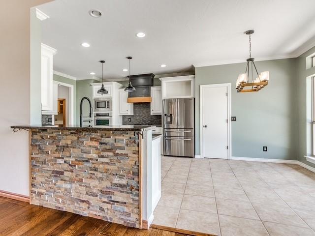 3805 Highridge, Edmond, OK 73003 - kitchen featuring appliances with stainless steel finishes, crown molding, backsplash, white cabinets, and a peninsula
