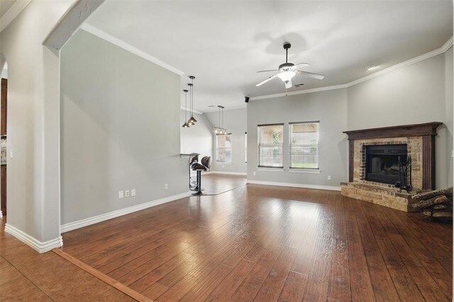 2716 Busheywood Dr, Yukon, OK 73099 - unfurnished living room featuring a fireplace, ceiling fan, dark wood-style flooring, ornamental molding, and arched walkways