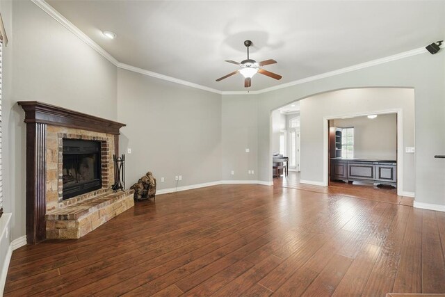 2716 Busheywood Dr, Yukon, OK 73099 - unfurnished living room featuring a ceiling fan, arched walkways, hardwood / wood-style floors, a brick fireplace, and crown molding