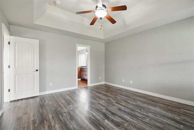 2716 Busheywood Dr, Yukon, OK 73099 - unfurnished bedroom featuring a raised ceiling, dark wood-style floors, connected bathroom, and ceiling fan