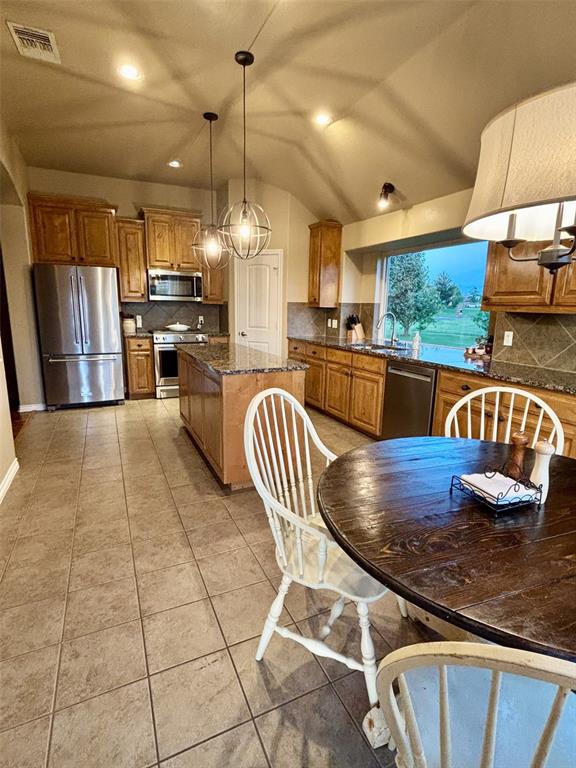 20301 Flowered Meadows Way, Edmond, OK 73012 - kitchen with stainless steel appliances, tasteful backsplash, brown cabinets, light tile patterned flooring, and decorative light fixtures
