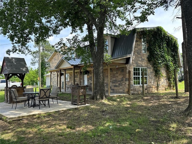 36166 Ew 1120th Rd, Seminole, OK 74868 - rear view of house with stone siding, a patio, a metal roof, and a standing seam roof