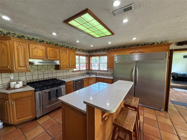 36166 Ew 1120th Rd, Seminole, OK 74868 - kitchen featuring appliances with stainless steel finishes, under cabinet range hood, a center island, a kitchen breakfast bar, and decorative backsplash