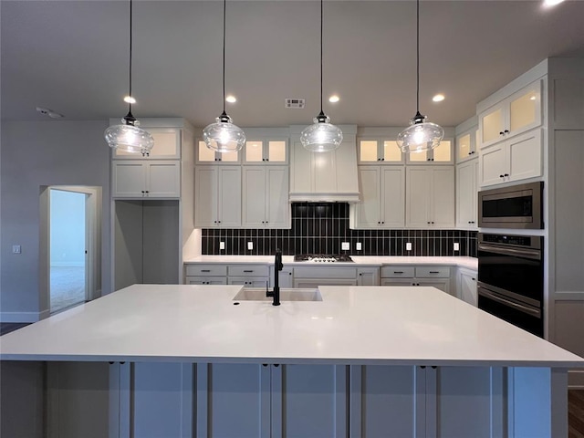 16405 Brookefield Dr, Edmond, OK 73013 - kitchen featuring stainless steel microwave, decorative backsplash, a large island with sink, white cabinets, and light countertops