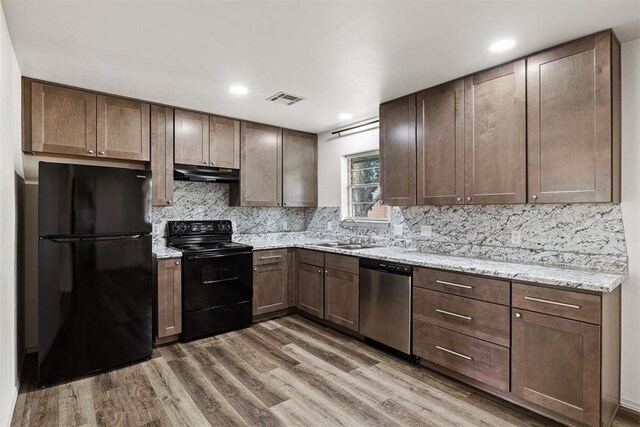 311 N Monroe Ave, Blanchard, OK 73010 - kitchen with black appliances, under cabinet range hood, wood finished floors, tasteful backsplash, and light stone countertops