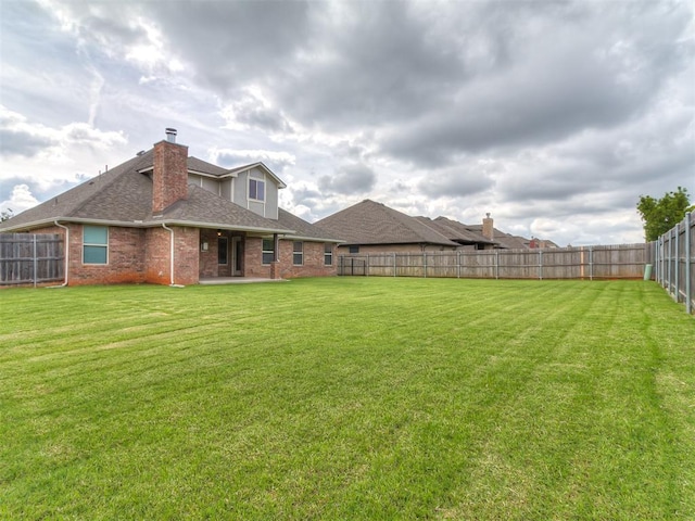 12917 Treemont Ln, Oklahoma City, OK 73142 - rear view of house featuring a fenced backyard, brick siding, roof with shingles, and a chimney