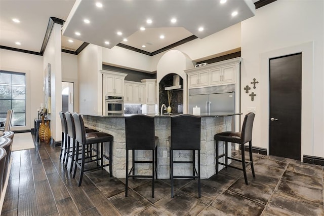 3617 Stagmoor Rd, Edmond, OK 73034 - kitchen featuring stainless steel appliances, crown molding, a breakfast bar, tasteful backsplash, and wall chimney range hood