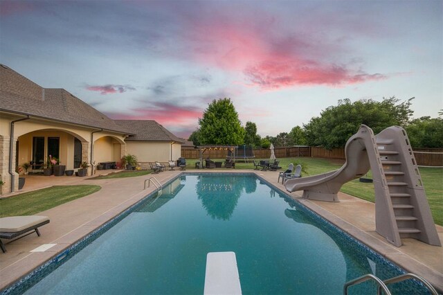 3617 Stagmoor Rd, Edmond, OK 73034 - pool at dusk featuring a water slide, a patio, a diving board, and a fenced backyard
