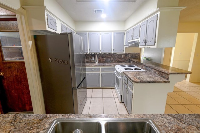 1383 N Peebly Rd, Choctaw, OK 73020 - kitchen with freestanding refrigerator, white range with electric cooktop, light tile patterned flooring, and a peninsula