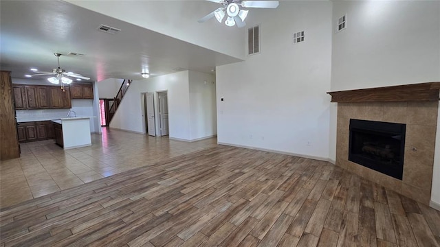 3441 NW 176th St, Edmond, OK 73012 - unfurnished living room featuring a ceiling fan, light wood-type flooring, a tiled fireplace, and a towering ceiling