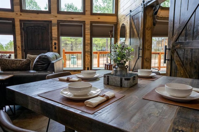 17 Honor Ct, Broken Bow, OK 74728 - dining room featuring a barn door, wood walls, wood finished floors, and a high ceiling