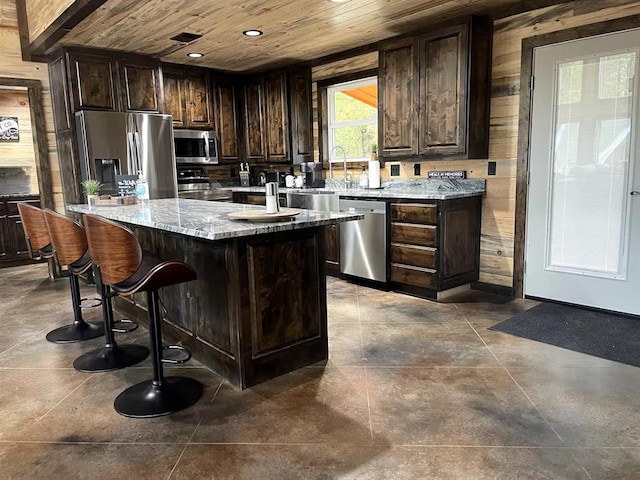 17 Honor Ct, Broken Bow, OK 74728 - kitchen with stainless steel appliances, wooden ceiling, wooden walls, dark brown cabinets, and a center island with sink