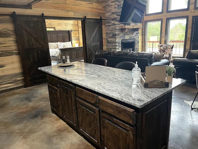 17 Honor Ct, Broken Bow, OK 74728 - kitchen with a barn door, wood walls, open floor plan, light stone counters, and dark brown cabinets