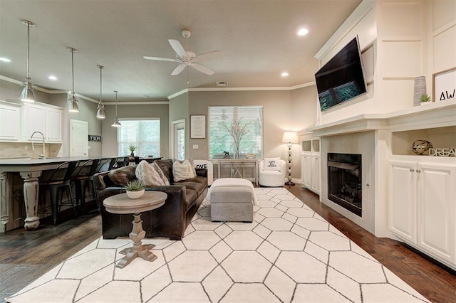 2473 Vellano Ln, Edmond, OK 73034 - living area featuring wood finished floors, a ceiling fan, recessed lighting, ornamental molding, and a tile fireplace