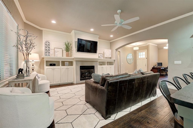 2473 Vellano Ln, Edmond, OK 73034 - living room with arched walkways, a ceiling fan, recessed lighting, ornamental molding, and a glass covered fireplace
