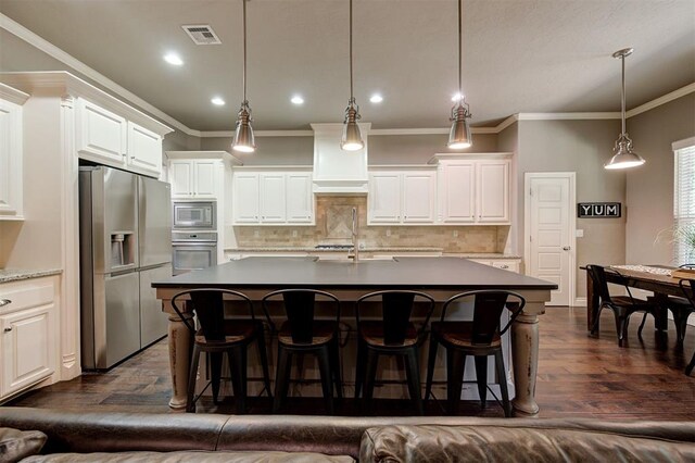 2473 Vellano Ln, Edmond, OK 73034 - kitchen featuring appliances with stainless steel finishes, tasteful backsplash, ornamental molding, a kitchen island with sink, and white cabinetry