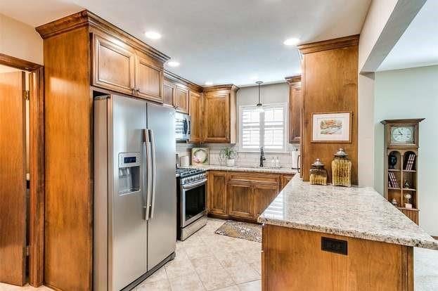 801 Belle Air Ave, Edmond, OK 73013 - kitchen featuring appliances with stainless steel finishes, a peninsula, brown cabinets, light stone countertops, and light tile patterned flooring