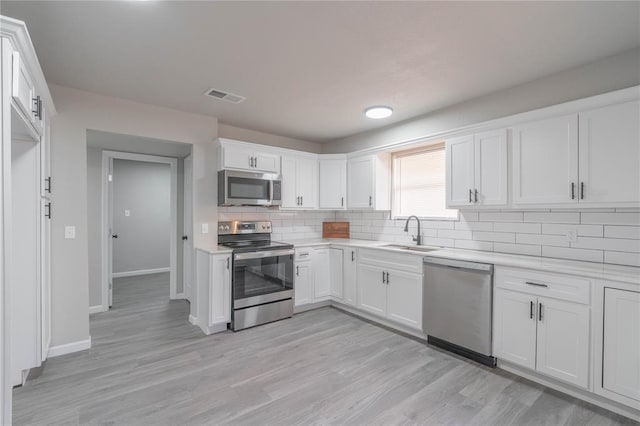 kitchen with stainless steel appliances, backsplash, light countertops, white cabinets, and light wood-style floors
