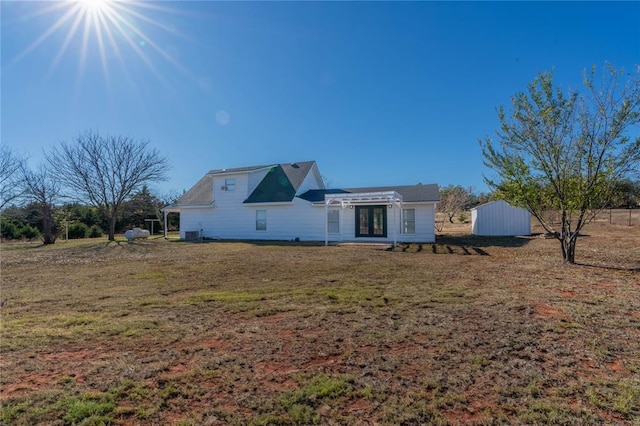 rear view of house with french doors, a storage unit, and a lawn