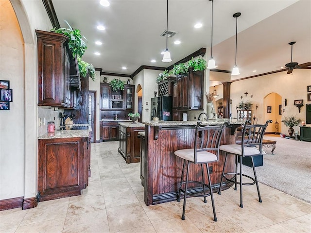 3705 Dalston Cir, Norman, OK 73072 - kitchen featuring arched walkways, freestanding refrigerator, crown molding, dark brown cabinetry, and a kitchen breakfast bar