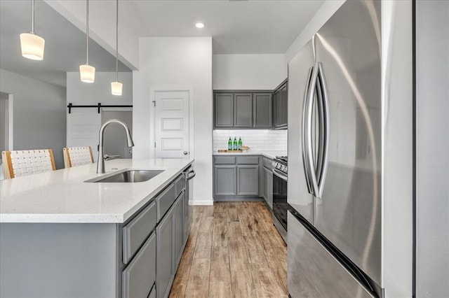 1108 Blackjack Creek Dr, Yukon, OK 73099 - kitchen with stainless steel appliances, gray cabinets, a barn door, light wood-style flooring, and a center island with sink