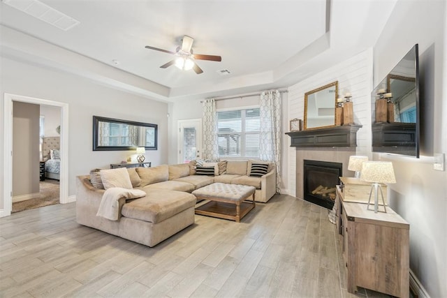 609 NW 180th St, Edmond, OK 73012 - living room featuring a tray ceiling, light wood-style flooring, ceiling fan, and a glass covered fireplace