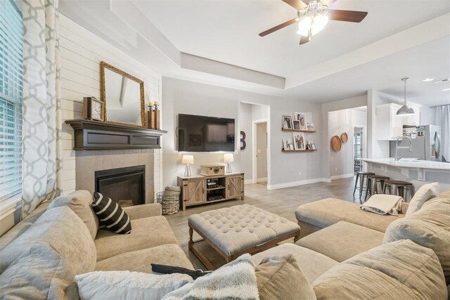 609 NW 180th St, Edmond, OK 73012 - living room featuring a ceiling fan, a tiled fireplace, a tray ceiling, and light wood finished floors