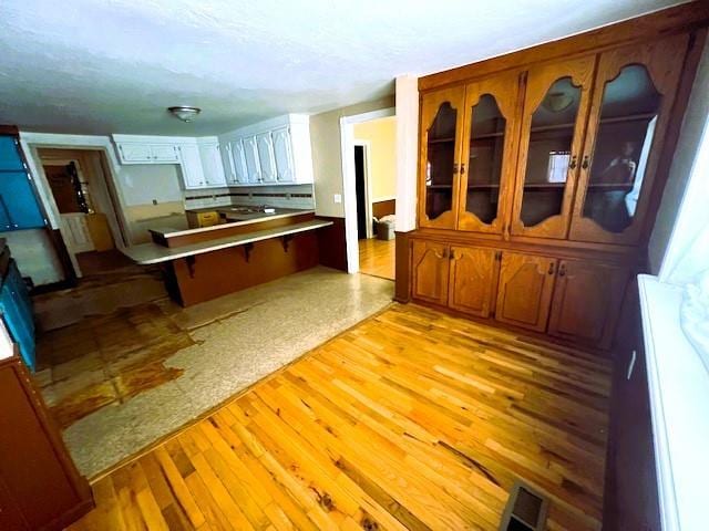 502 E Cavalry St, Cordell, OK 73632 - kitchen with a peninsula, light wood-style flooring, glass insert cabinets, and a breakfast bar