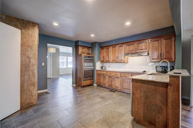 3208 NW 47th St, Oklahoma City, OK 73112 - kitchen with double oven, a peninsula, brown cabinets, light stone countertops, and tasteful backsplash