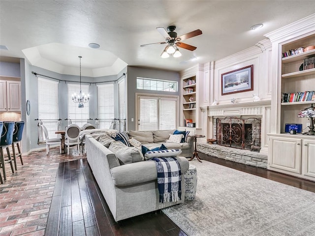 4304 Riders Mark, Edmond, OK 73025 - living room featuring a chandelier, a ceiling fan, a stone fireplace, built in features, and dark wood-type flooring