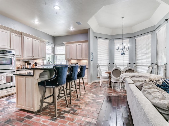 4304 Riders Mark, Edmond, OK 73025 - kitchen with double oven, a chandelier, a breakfast bar area, backsplash, and brick floors