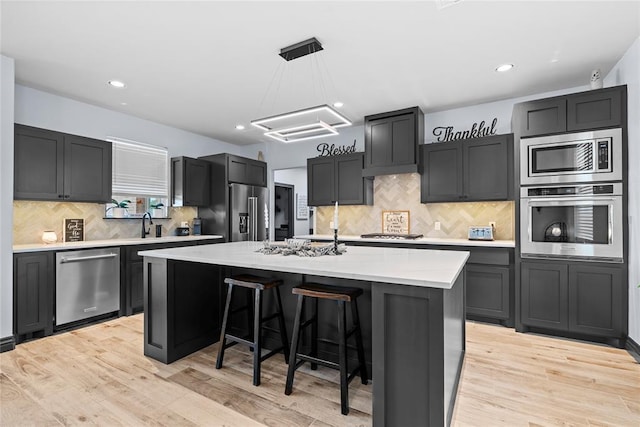 1031 Colonial Ave, Tuttle, OK 73089 - kitchen featuring appliances with stainless steel finishes, decorative backsplash, a breakfast bar, an island with sink, and recessed lighting