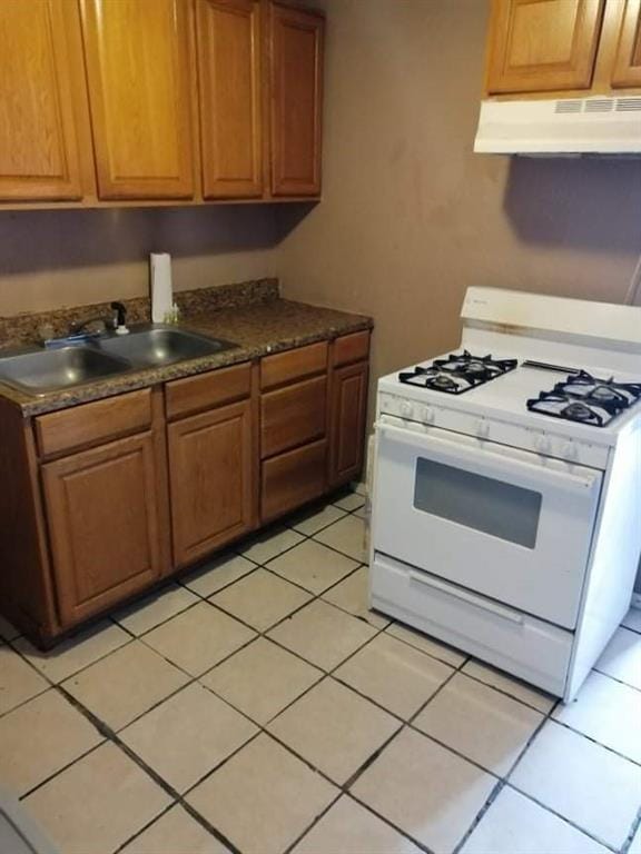 2904 S Indiana Ave, Oklahoma City, OK 73108 - kitchen featuring white gas stove, ventilation hood, dark countertops, light tile patterned floors, and brown cabinetry