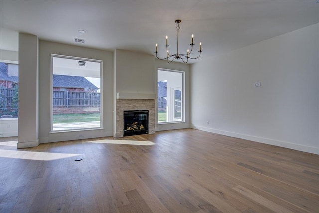 2006 Ithaca Dr, Norman, OK 73071 - unfurnished living room featuring a chandelier, healthy amount of natural light, wood finished floors, and a stone fireplace