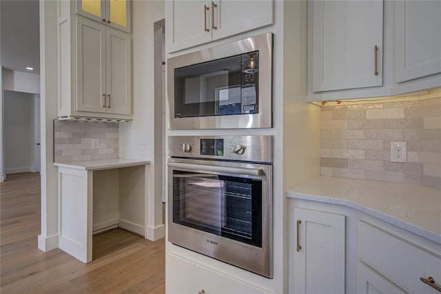 2006 Ithaca Dr, Norman, OK 73071 - kitchen featuring stainless steel oven, built in microwave, light wood-style flooring, tasteful backsplash, and light stone countertops
