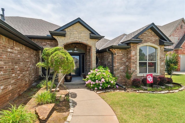 1600 SW 123rd St, Oklahoma City, OK 73170 - doorway to property with a shingled roof, brick siding, a lawn, and stone siding