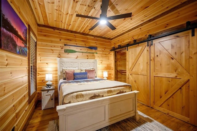 64 Mountain Alder Trl, Broken Bow, OK 74728 - bedroom with a barn door, wooden walls, wood ceiling, wood finished floors, and a ceiling fan