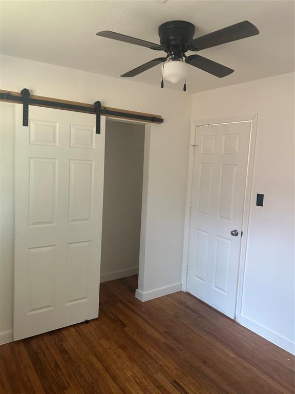 5326 NW Columbia Ave, Lawton, OK 73505 - unfurnished bedroom with a barn door, dark wood-style flooring, a closet, and a ceiling fan