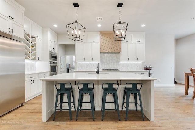 5017 Yale Bridge Ct, Edmond, OK 73034 - kitchen with built in appliances, a chandelier, tasteful backsplash, an island with sink, and light wood-style flooring